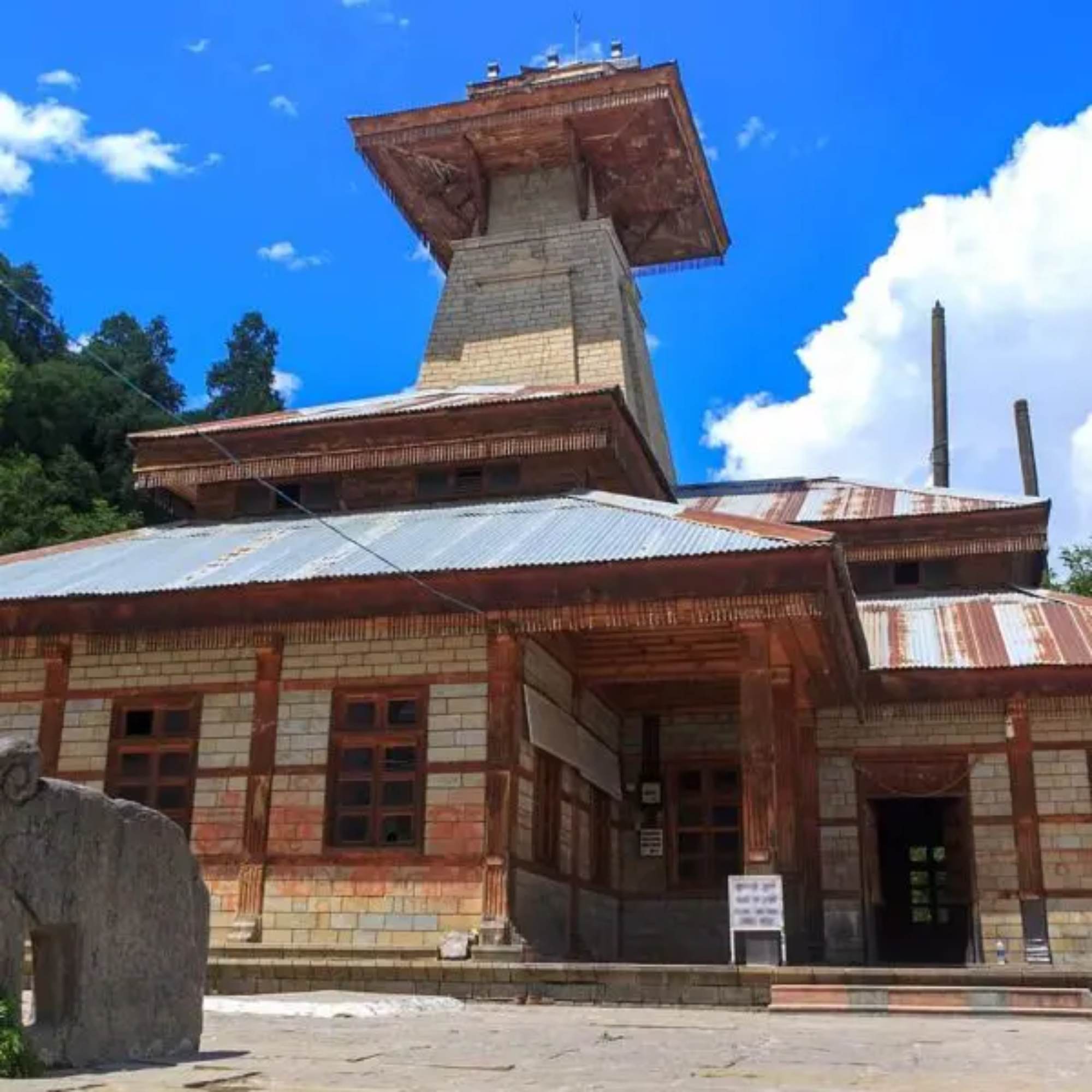 Peaceful view of Manu Temple with deodar trees and mountain backdrop in Old Manali
